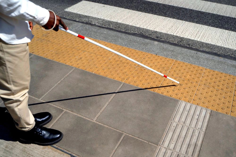 Image of a person with a white cane navigating using a tactile pavement